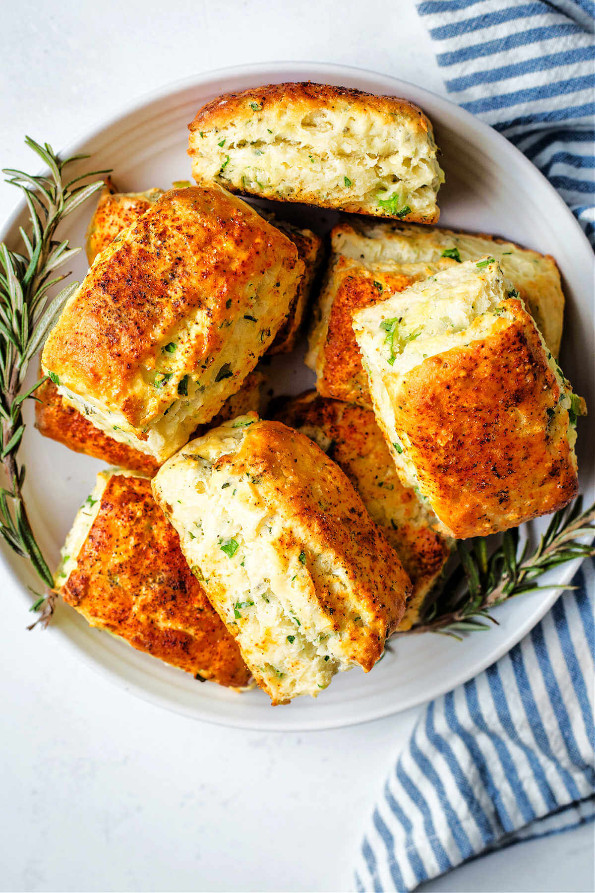 Savory scones piled on a plate with sprigs of rosemary on a table.