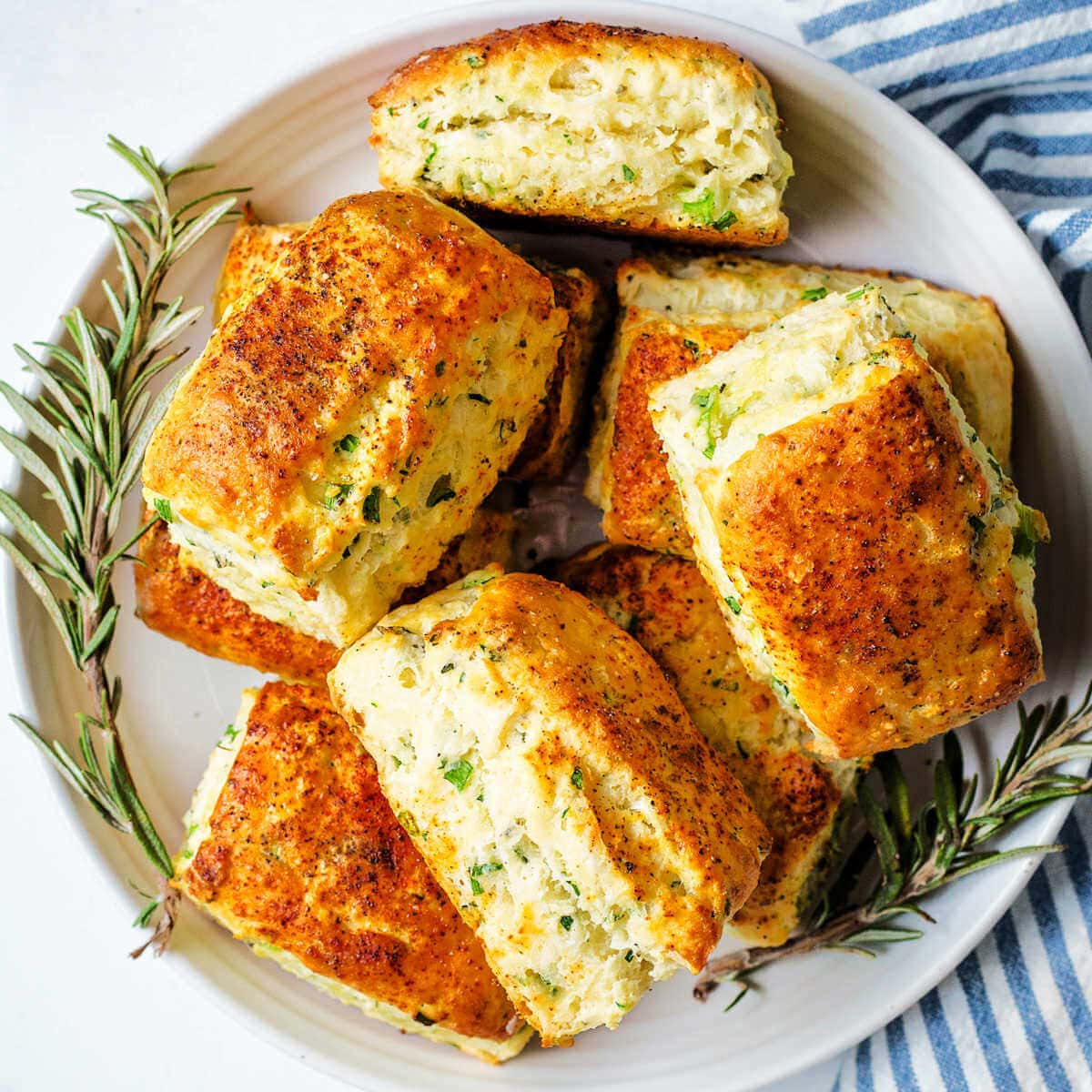 Savory scones piled on a plate with sprigs of rosemary on a table.