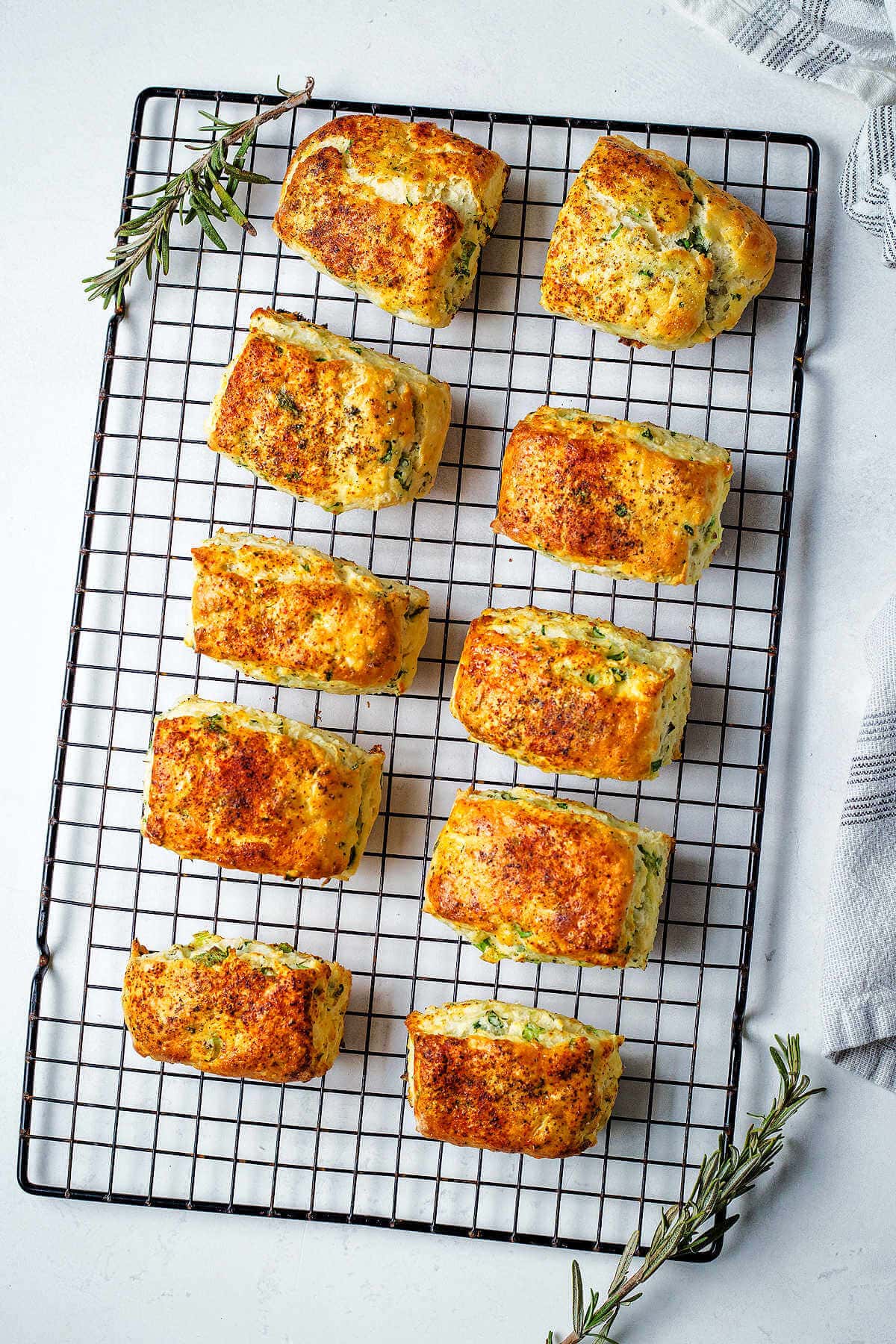 Savory ricotta scones cooling on a wire rack with sprigs of rosemary.