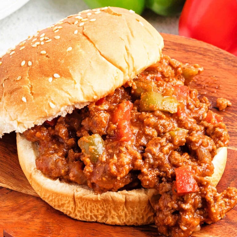 Sloppy Joe sandwich meat spilling over on a split hamburger bun on a wooden board on a table.