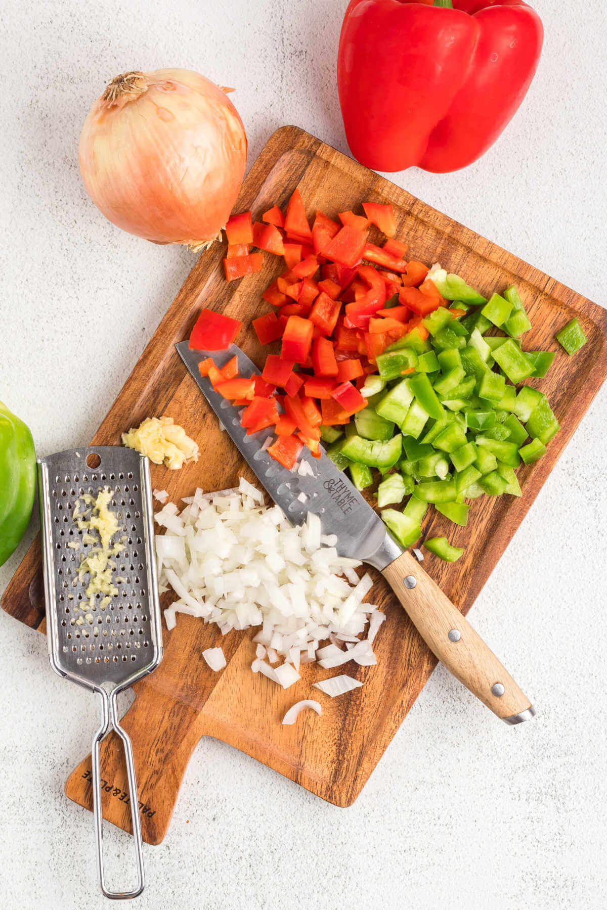 Bell peppers and onions diced on a cutting board on a table.