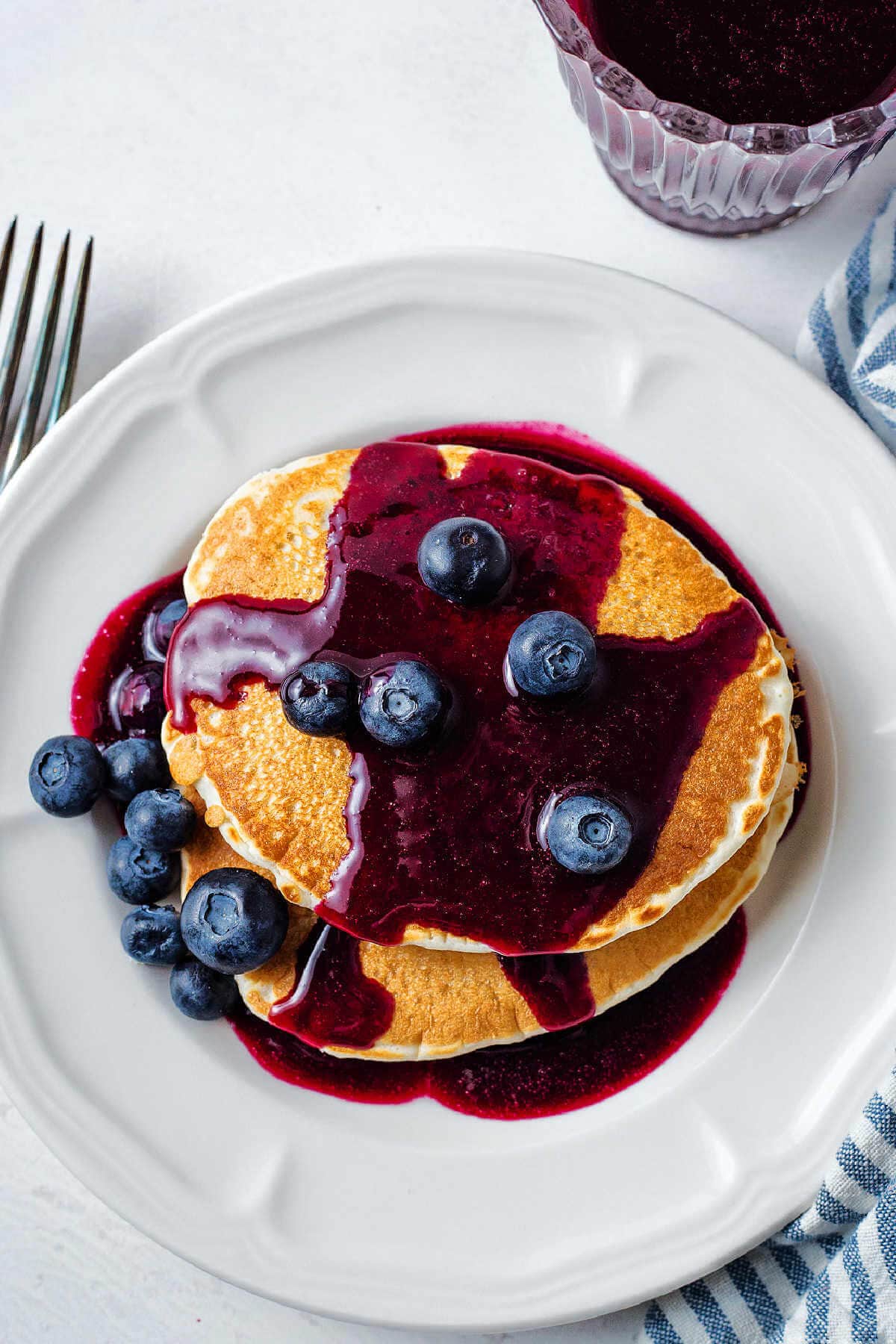 A stack of pancakes doused with blueberry syrup and blueberries on a table.