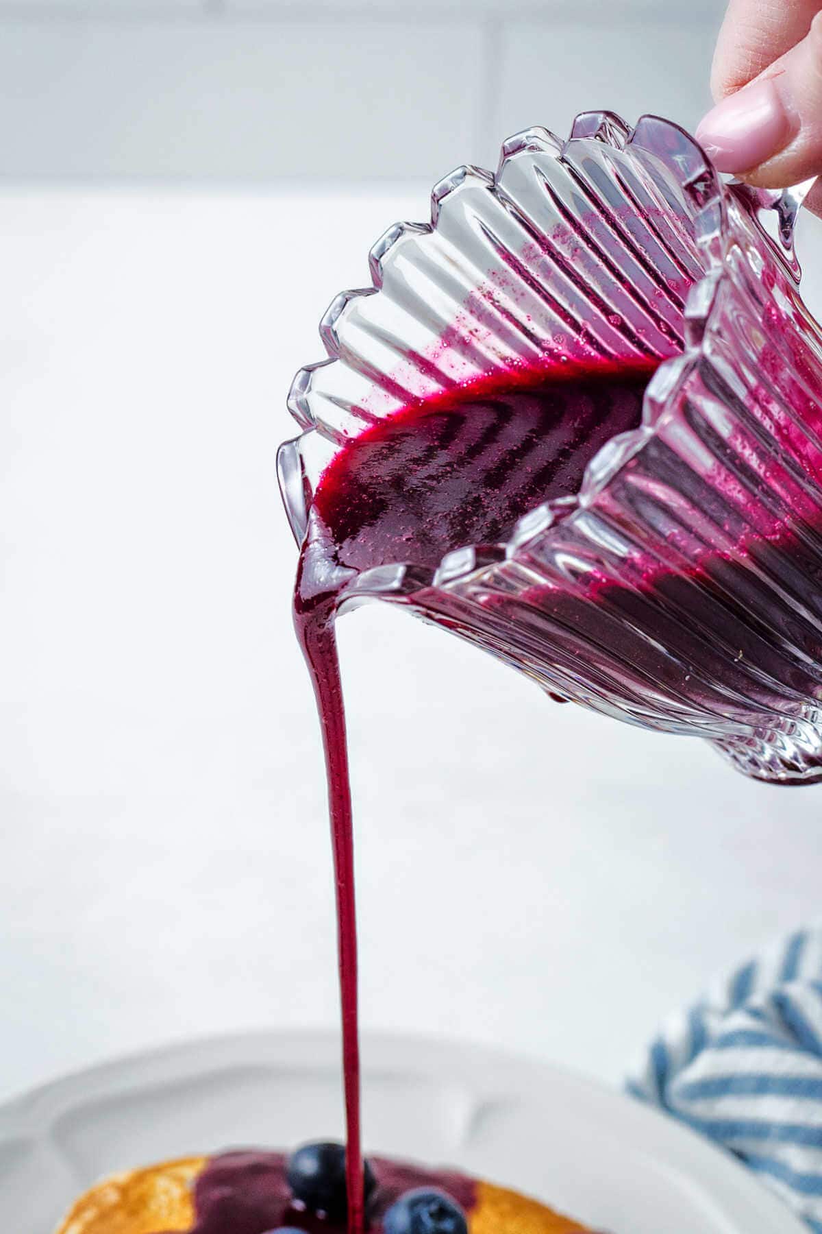 Pouring blueberry syrup onto pancakes from a decorative pitcher.