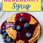 A stack of pancakes doused with blueberry syrup and blueberries on a table.