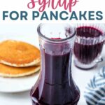 Blueberry syrup in a carafe on a table with a plate of pancakes.