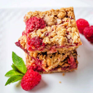 Raspberry bars stacked on a serving plate garnished with fresh mint.