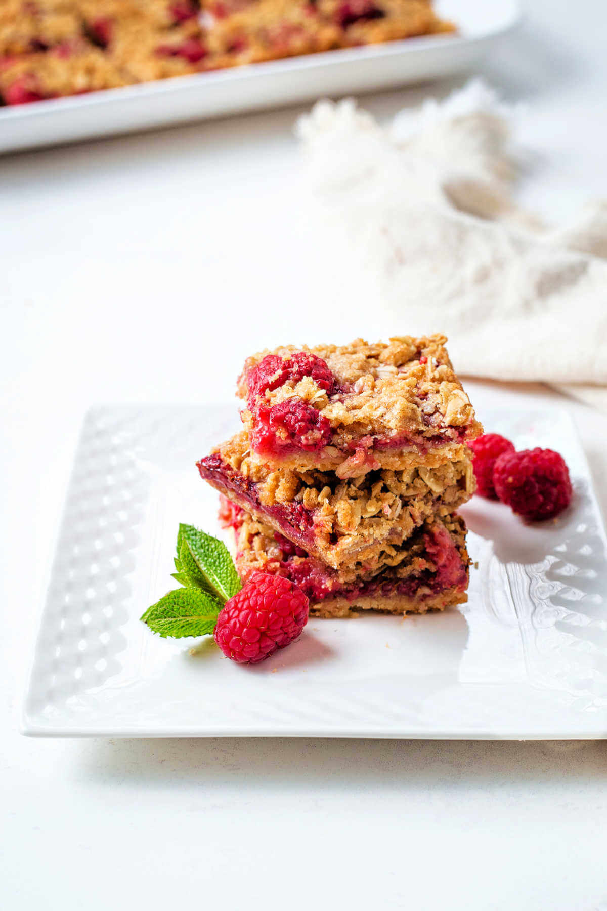 Raspberry bars stacked on a serving plate garnished with fresh mint.