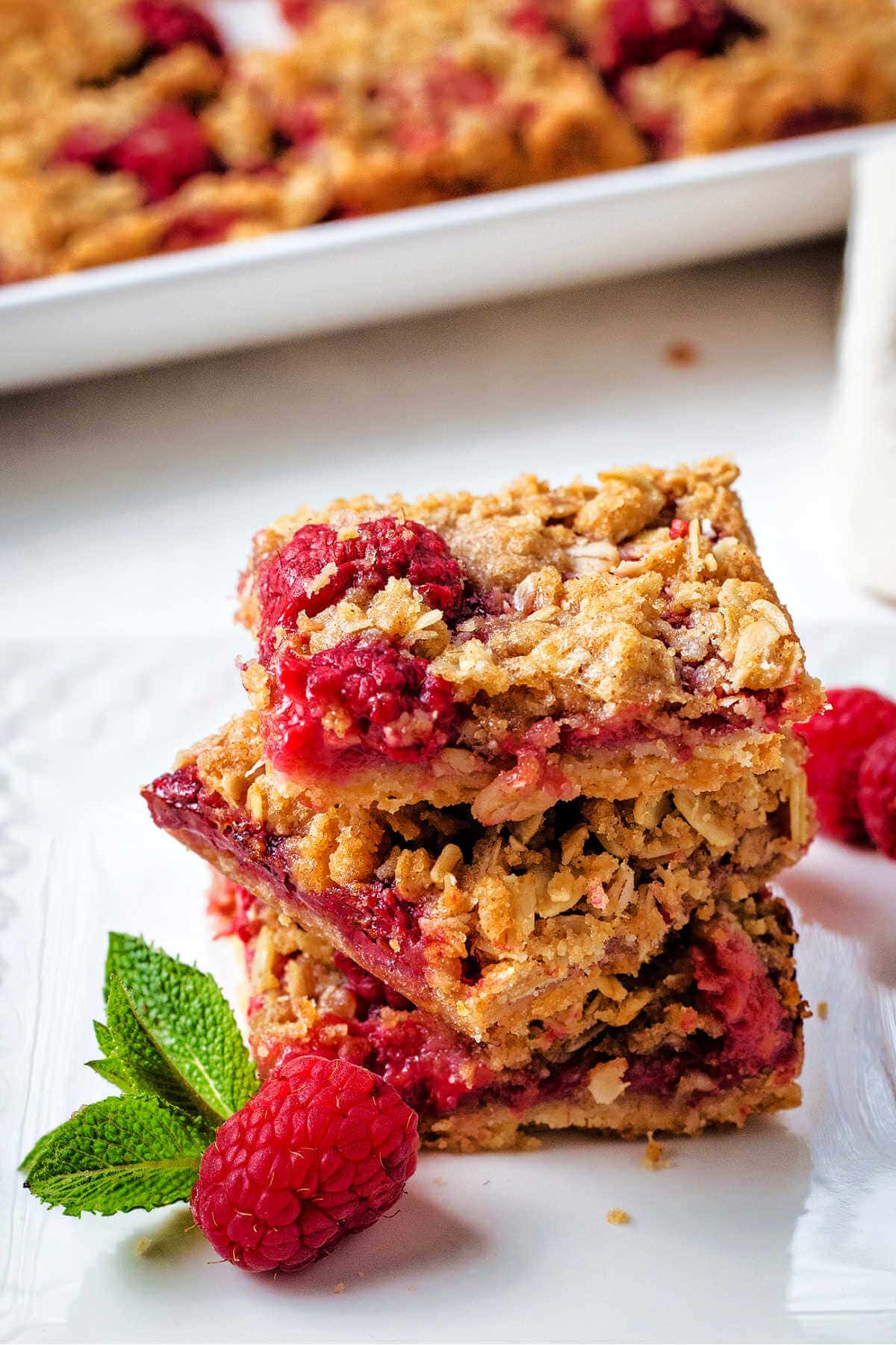 A stack of raspberry oatmeal bars on a plate on a table with a platter in the background.