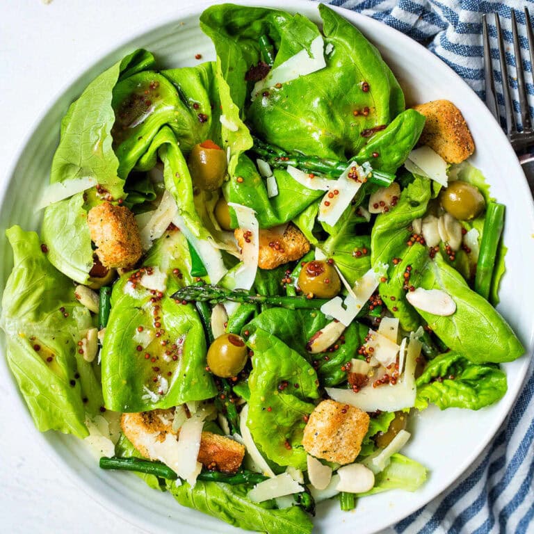 Overhead shot of butter lettuce salad with asparagus and olives and whole grain mustard dressing on top.