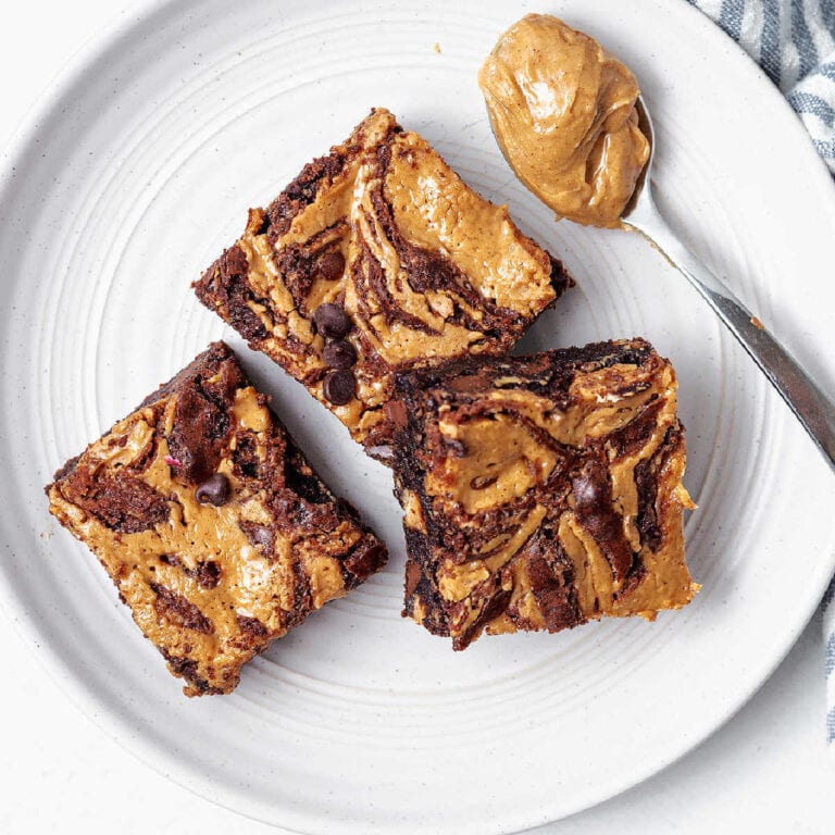 Overhead shot of three peanut butter brownies on a plate next to a spoon of peanut butter.