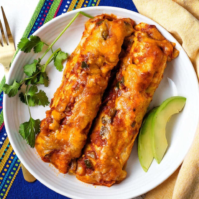 Chicken Black Bean enchiladas on a plate with avocado slices and sprigs of cilantro.