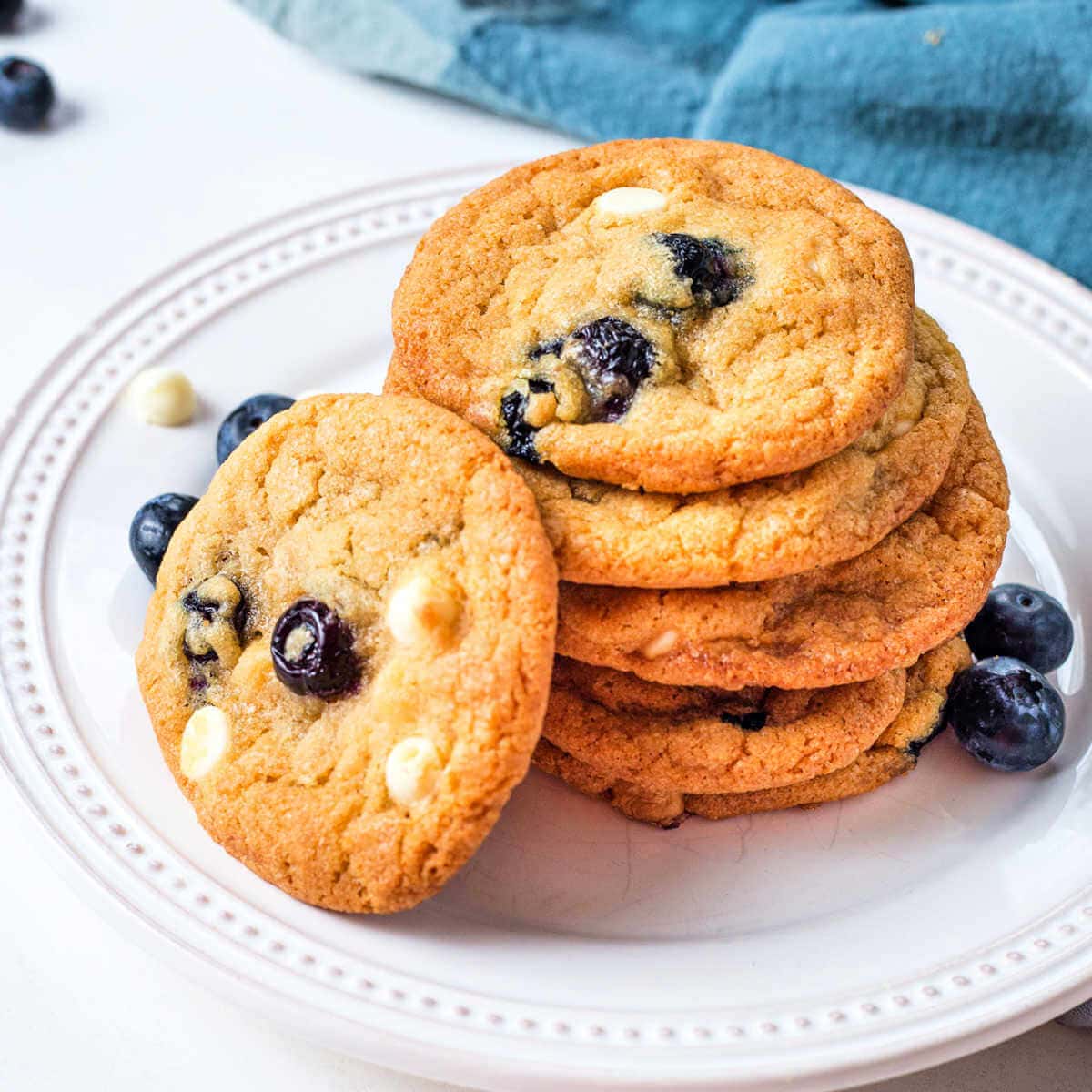 Blueberry Cookies with white chocolate chips stacked on a plate on a table.