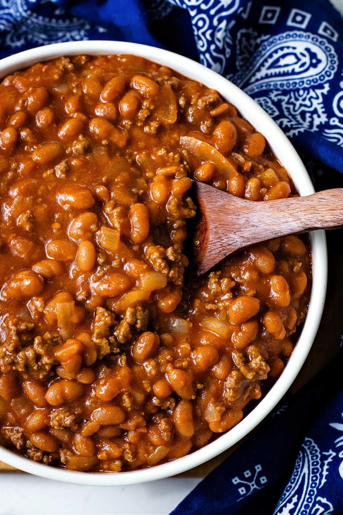 Cowboy beans in a large serving bowl with a wooden spoon.