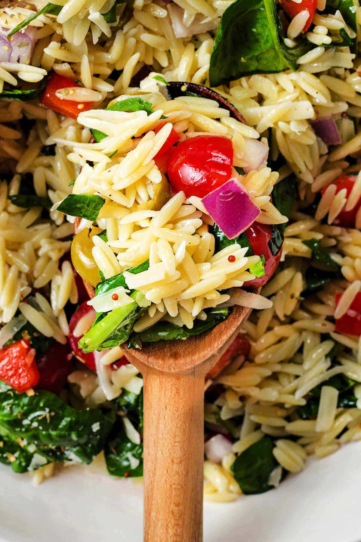 Greek orzo pasta salad in a bowl with a wooden spoon scooping some up.