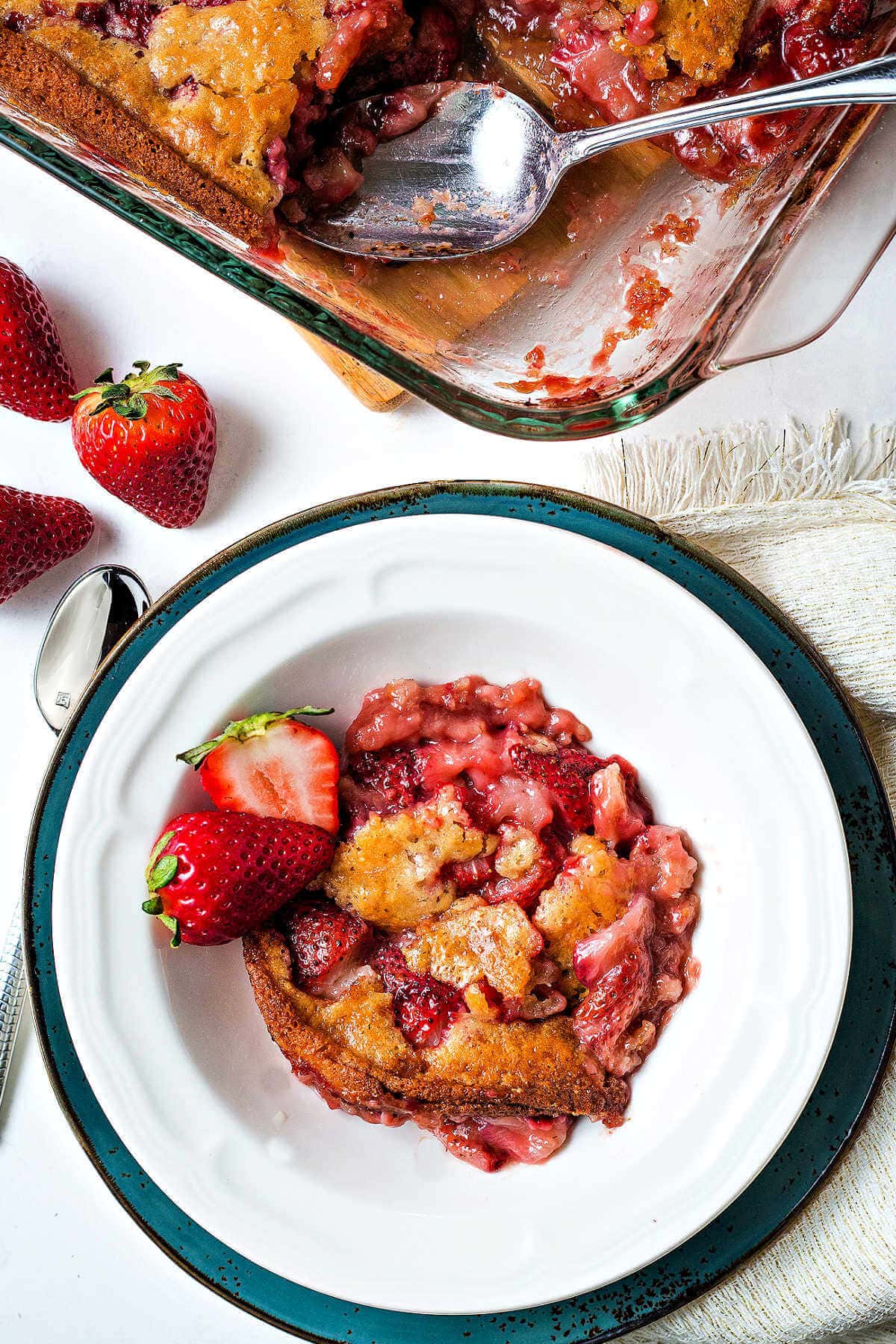 Strawberry cobbler in a bowl next to the baking dish of cobbler.