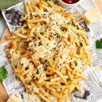 Truffle Fries with parmesan cheese and parsley on a newspaper lined board.