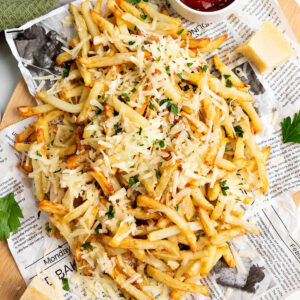 Truffle Fries with parmesan cheese and parsley on a newspaper lined board.