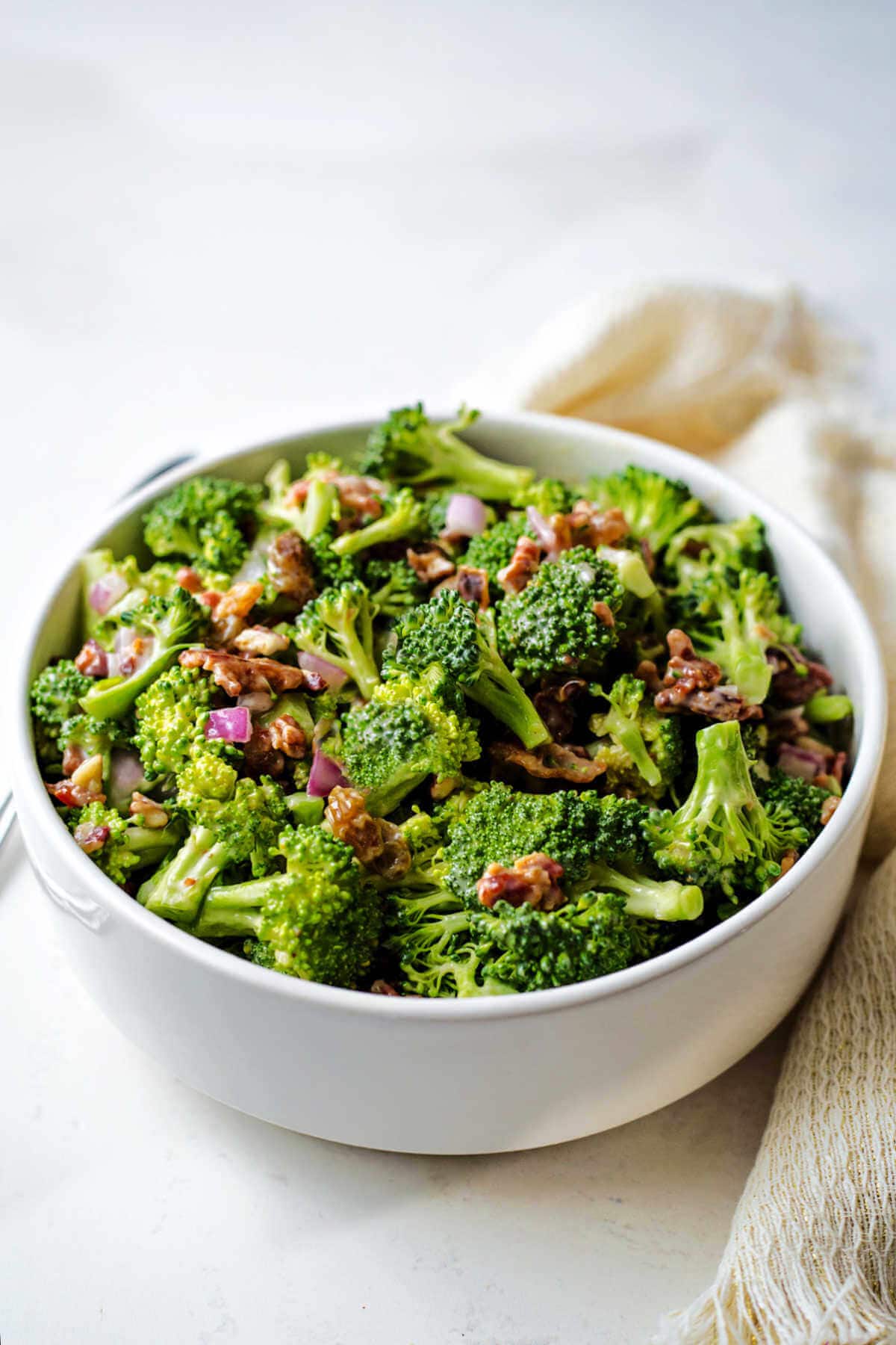 Side view of a broccoli salad served in a white bowl.
