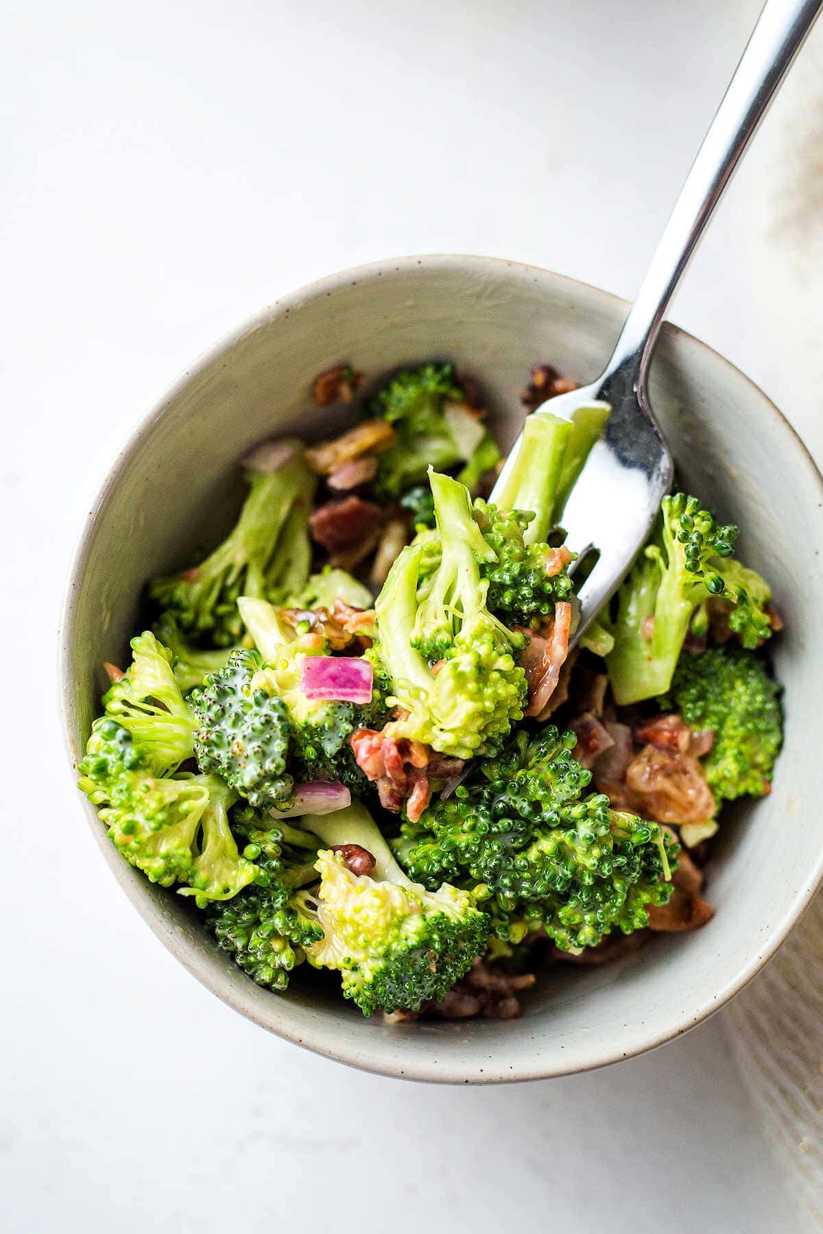 A bowl of broccoli salad with a fork inserted.