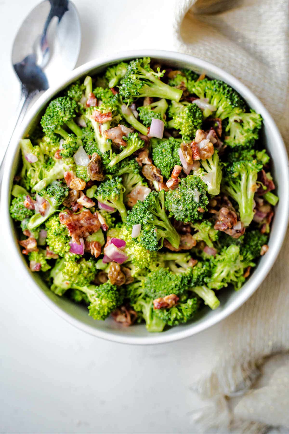 Broccoli Salad with Golden Raisins, pecans, and bacon in a serving bowl on a table.
