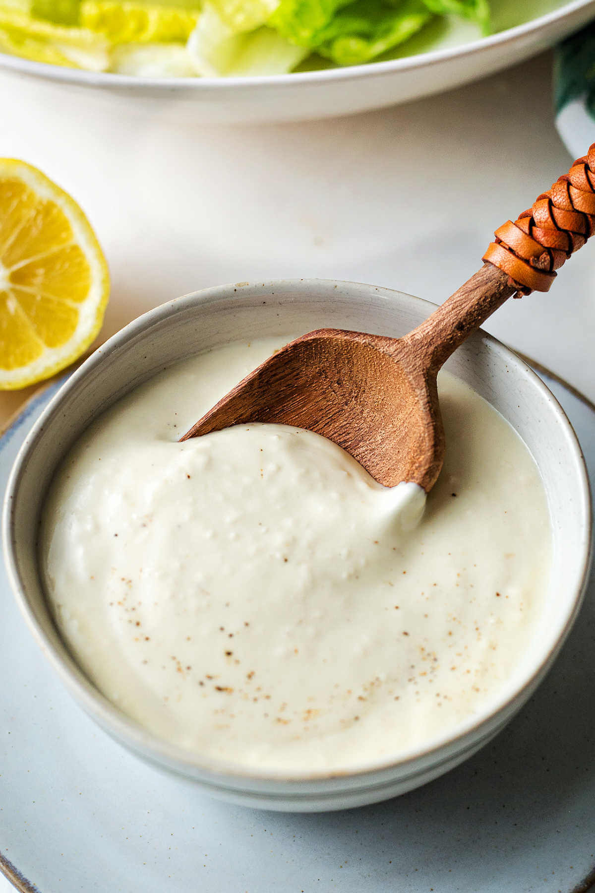 Greek yogurt Caesar salad dressing served in a bowl with a wooden spoon.