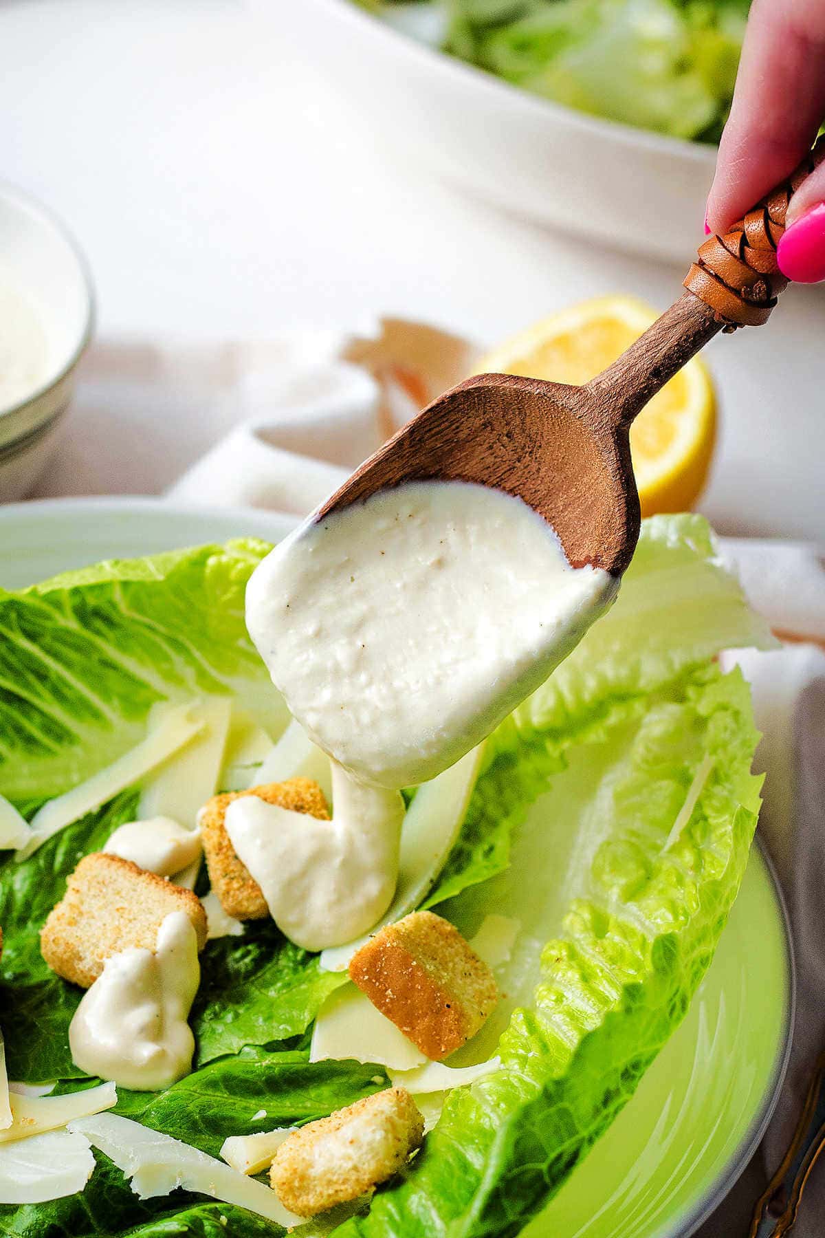 Using a wooden spoon to drizzle the caesar dressing onto a caesar salad.