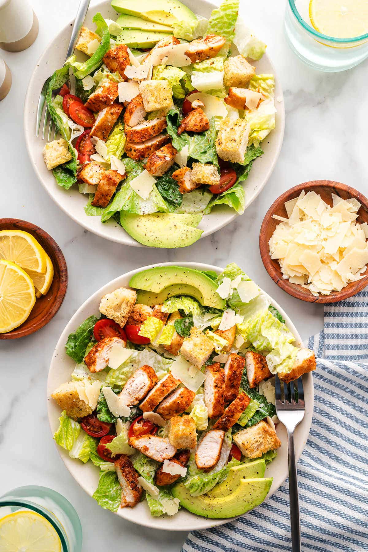 Chicken Caesar Salad divided between two plates on a table with napkins and forks.