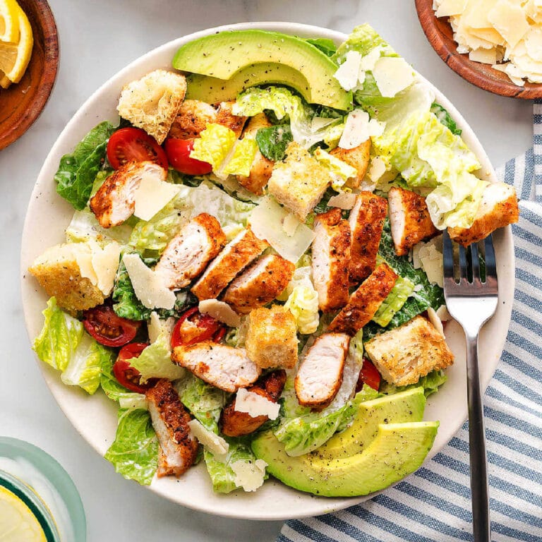 Chicken Caesar Salad garnished with sliced avocados on a plate.