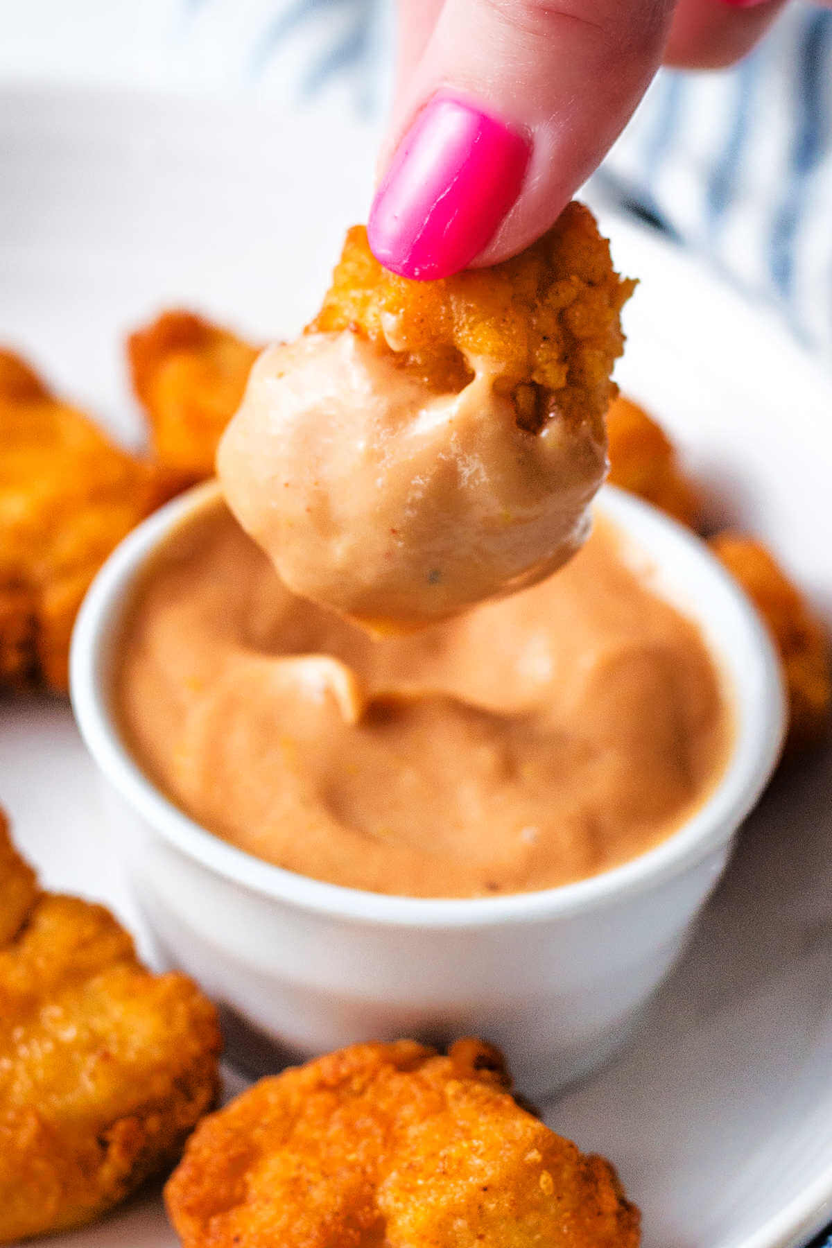Hand dipping a chicken nugget into a ramekin of chickfil-A sauce.