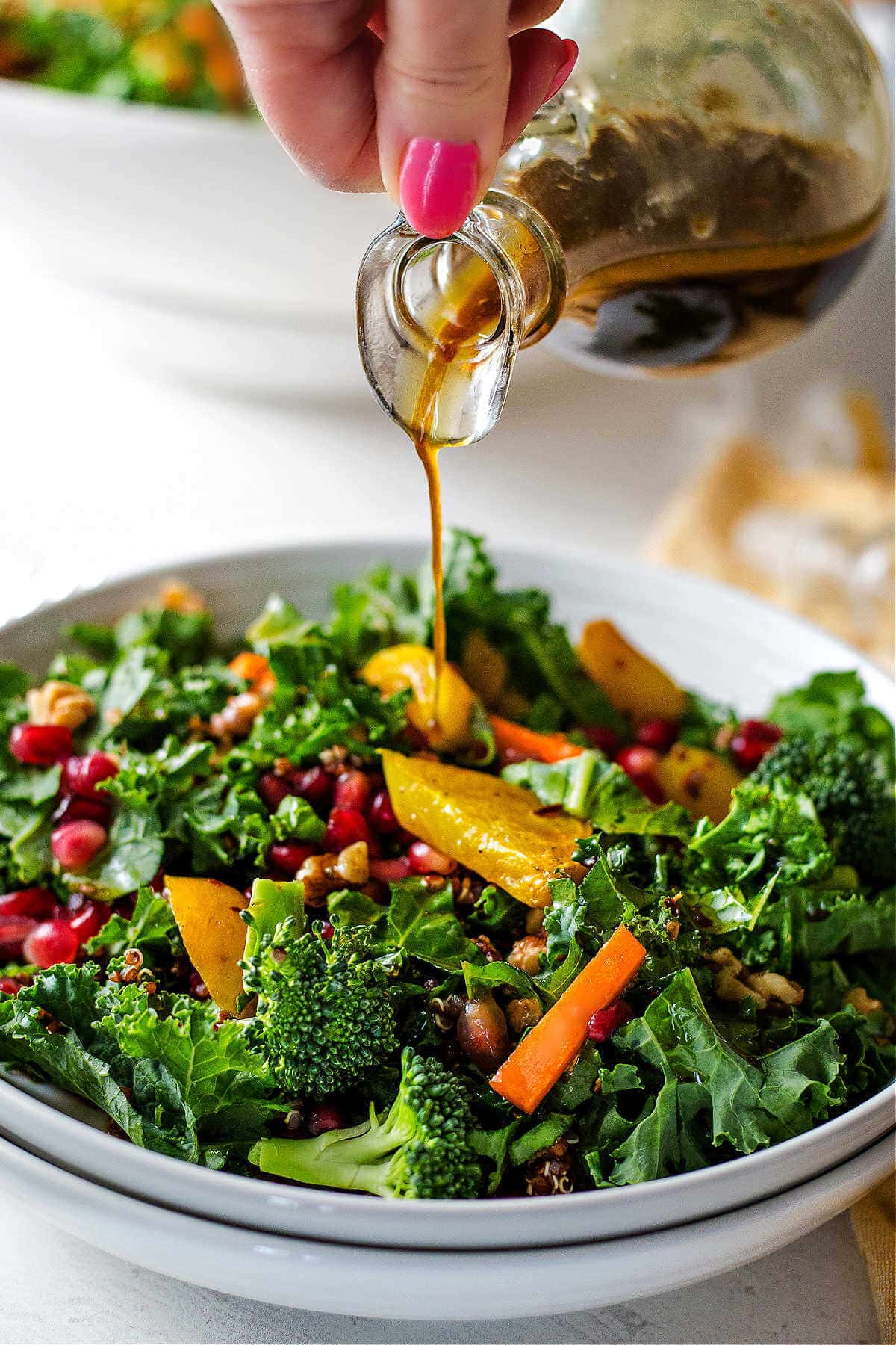 Hand pouring the ginger sesame dressing onto the salad in a bowl.