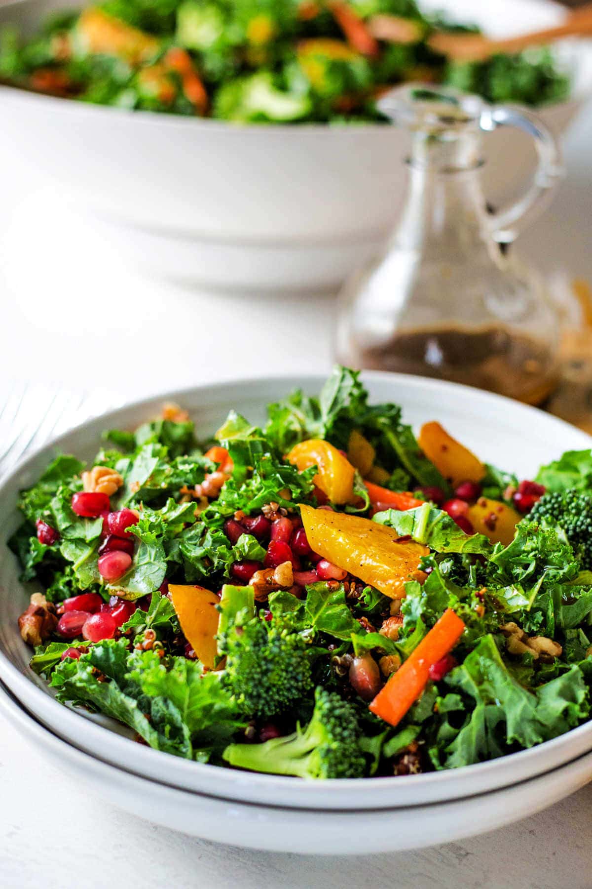 Dressed salad in a bowl stacked on top of another bowl with a large salad in the background.