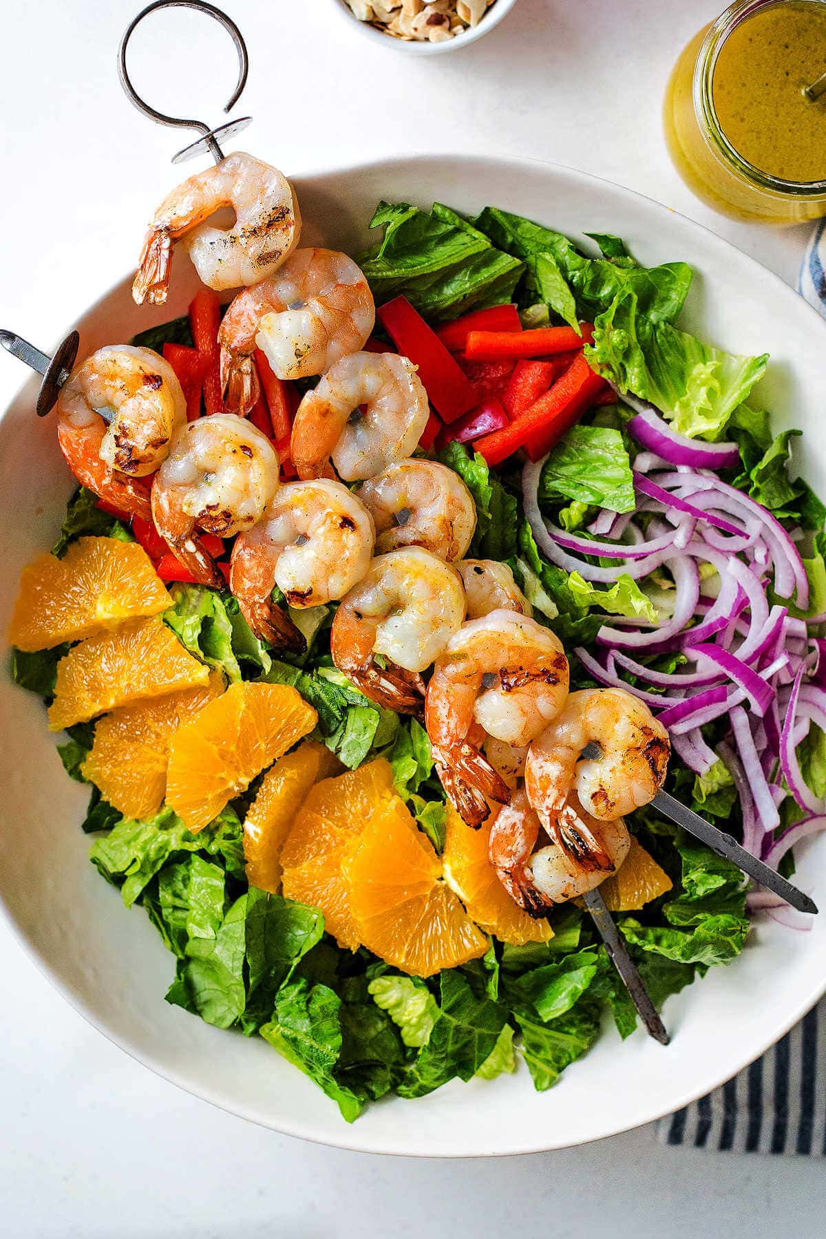 Salad in a white bowl with grilled shrimp skewers on top.