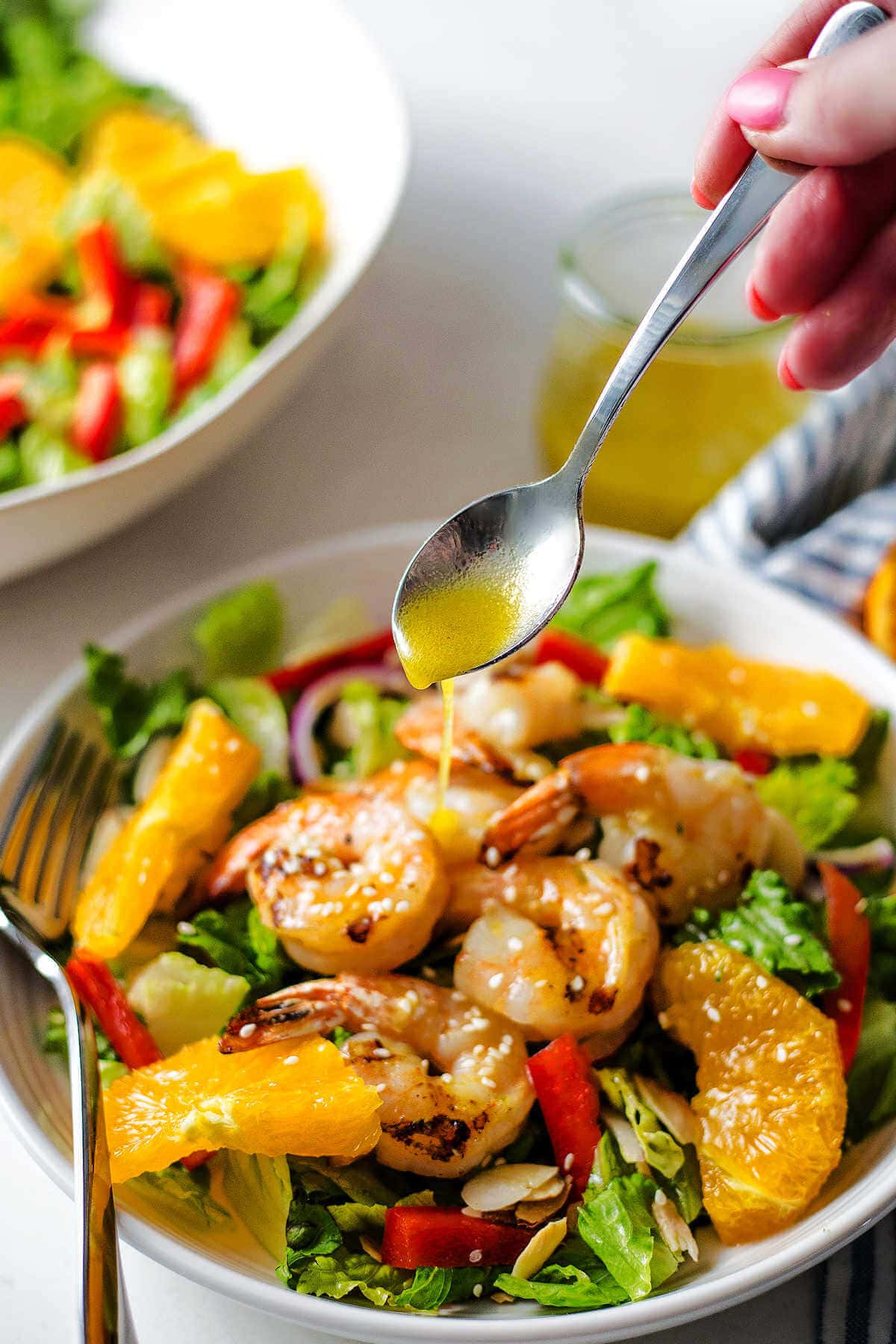 Hand spooning the homemade citrus vinaigrette onto the grilled shrimp salad.