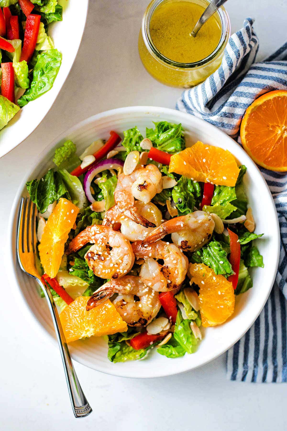Overhead shot of grilled shrimp salad in a bowl next to the jar of dressing.