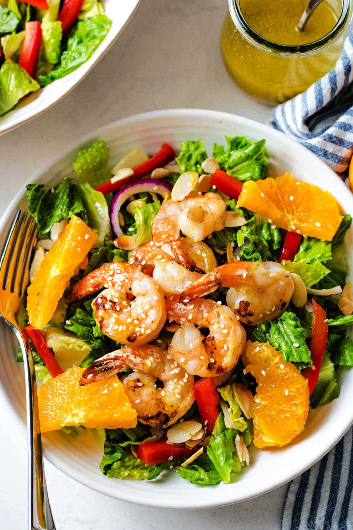 Grilled shrimp salad with citrus vinaigrette in a white bowl with a fork.