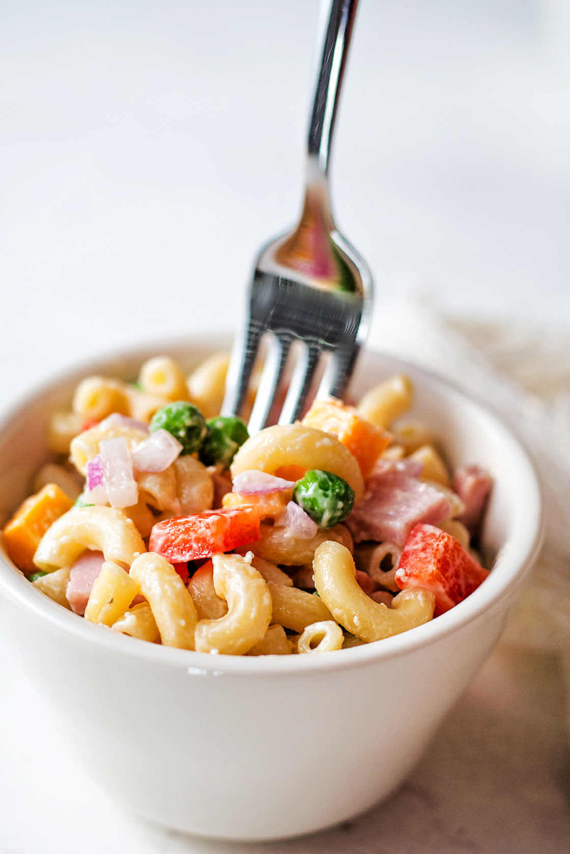 Creamy macaroni salad with peas in a small white bowl with a fork.