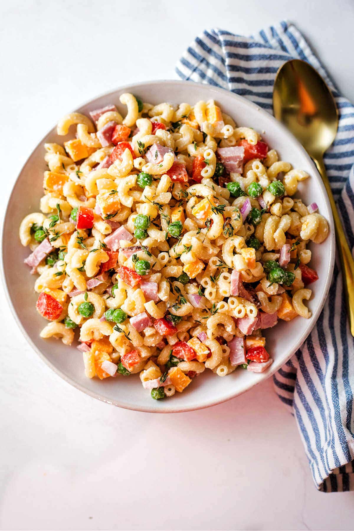 Macaroni salad with peas served in a bowl with a napkin and spoon on the side.