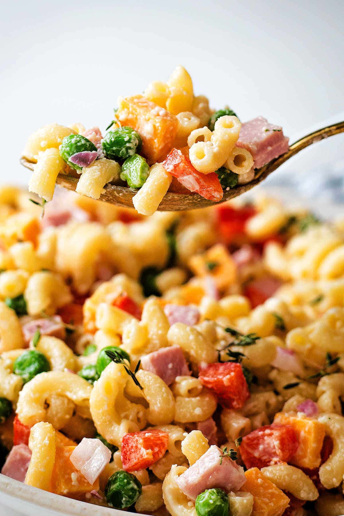 Spoon of macaroni salad hovering over a bowl of salad.