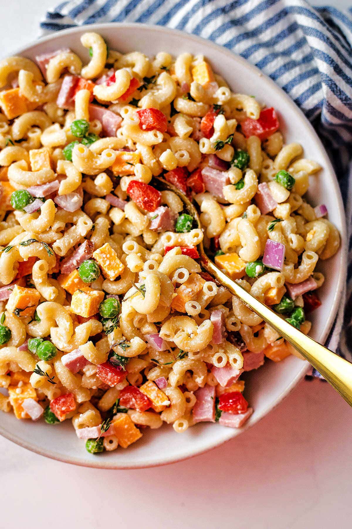 Creamy macaroni salad with peas served in a white bowl with a gold spoon.