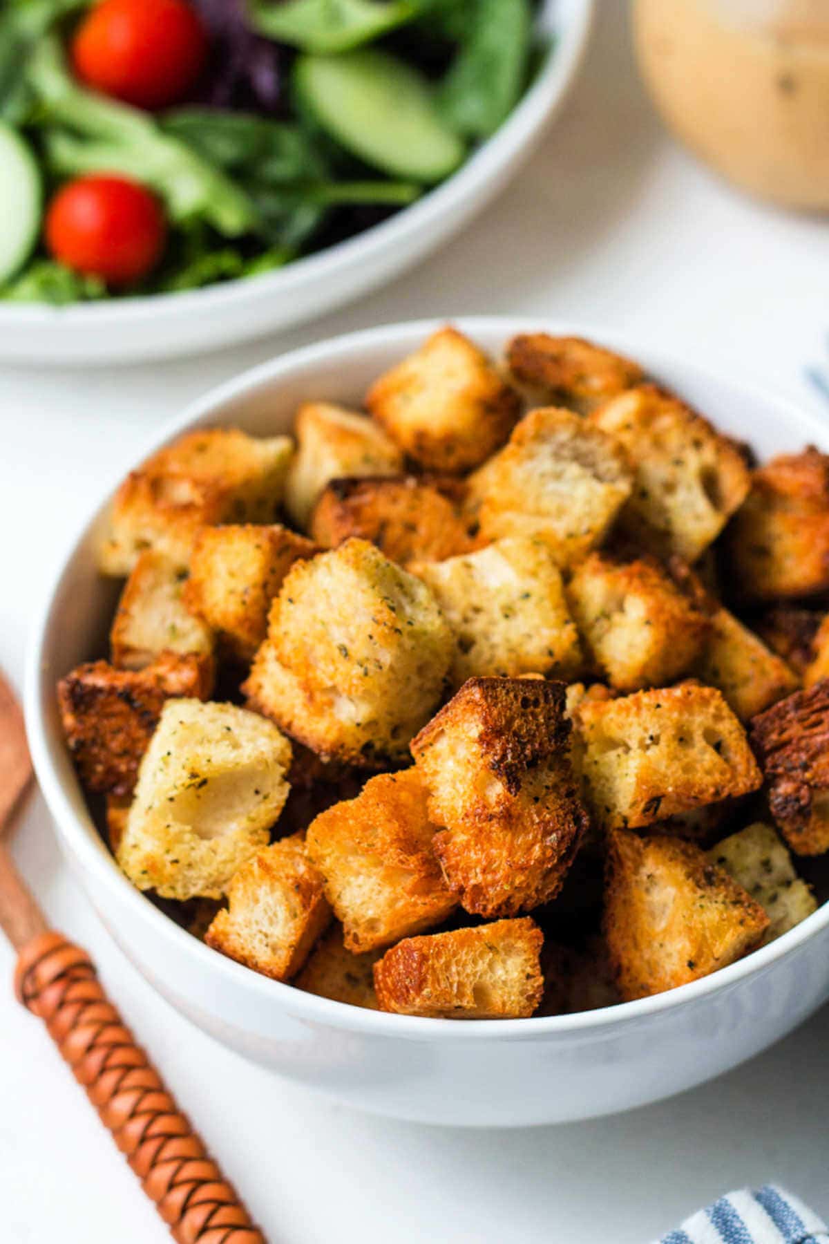 Bowl of homemade croutons in a bowl with a salad in the background.
