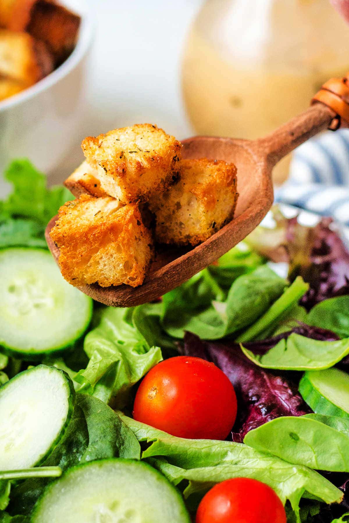 Wooden spoon with croutons on them hovering over a green salad.