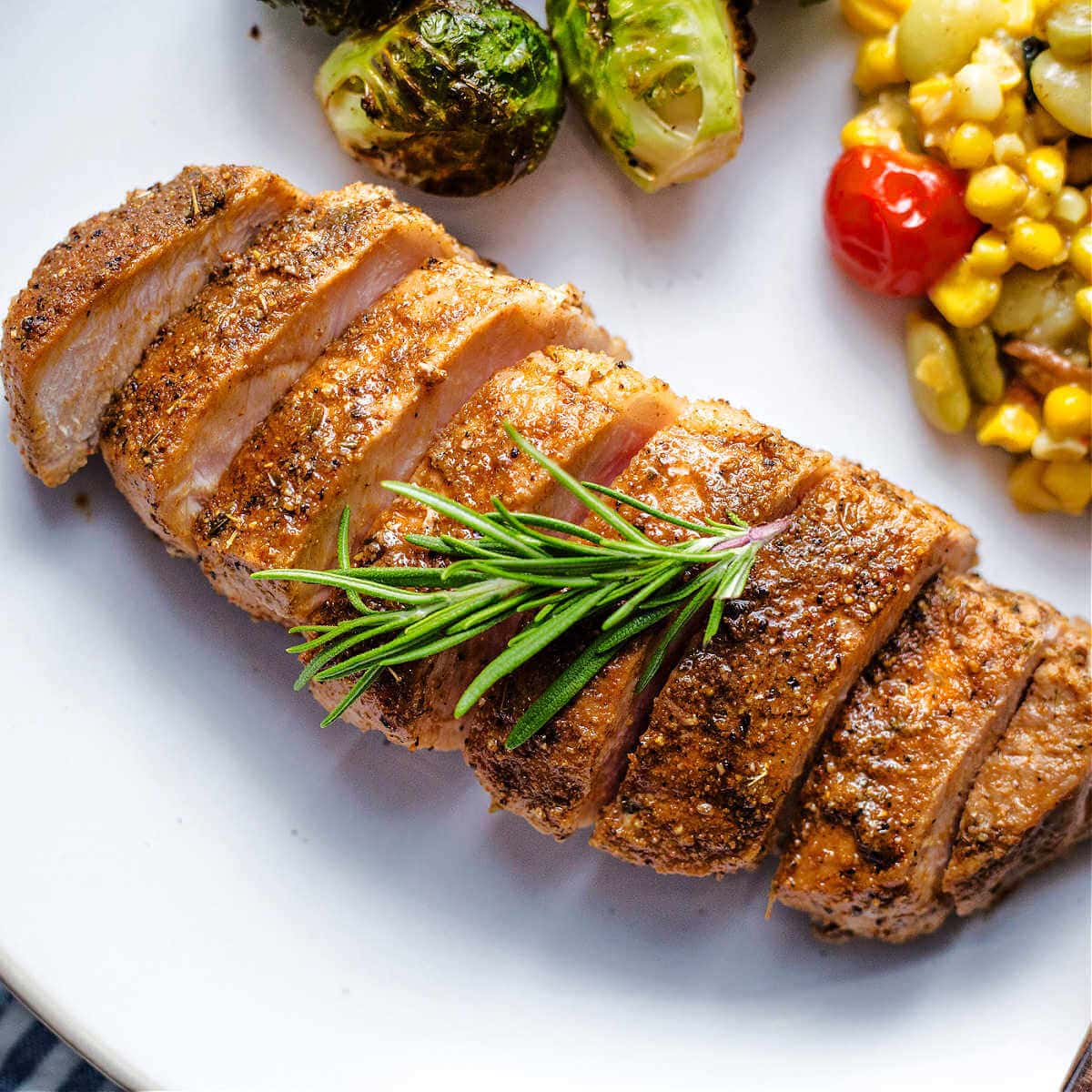 A baked boneless pork loin chop sliced and on a plate garnished with a rosemary sprig.