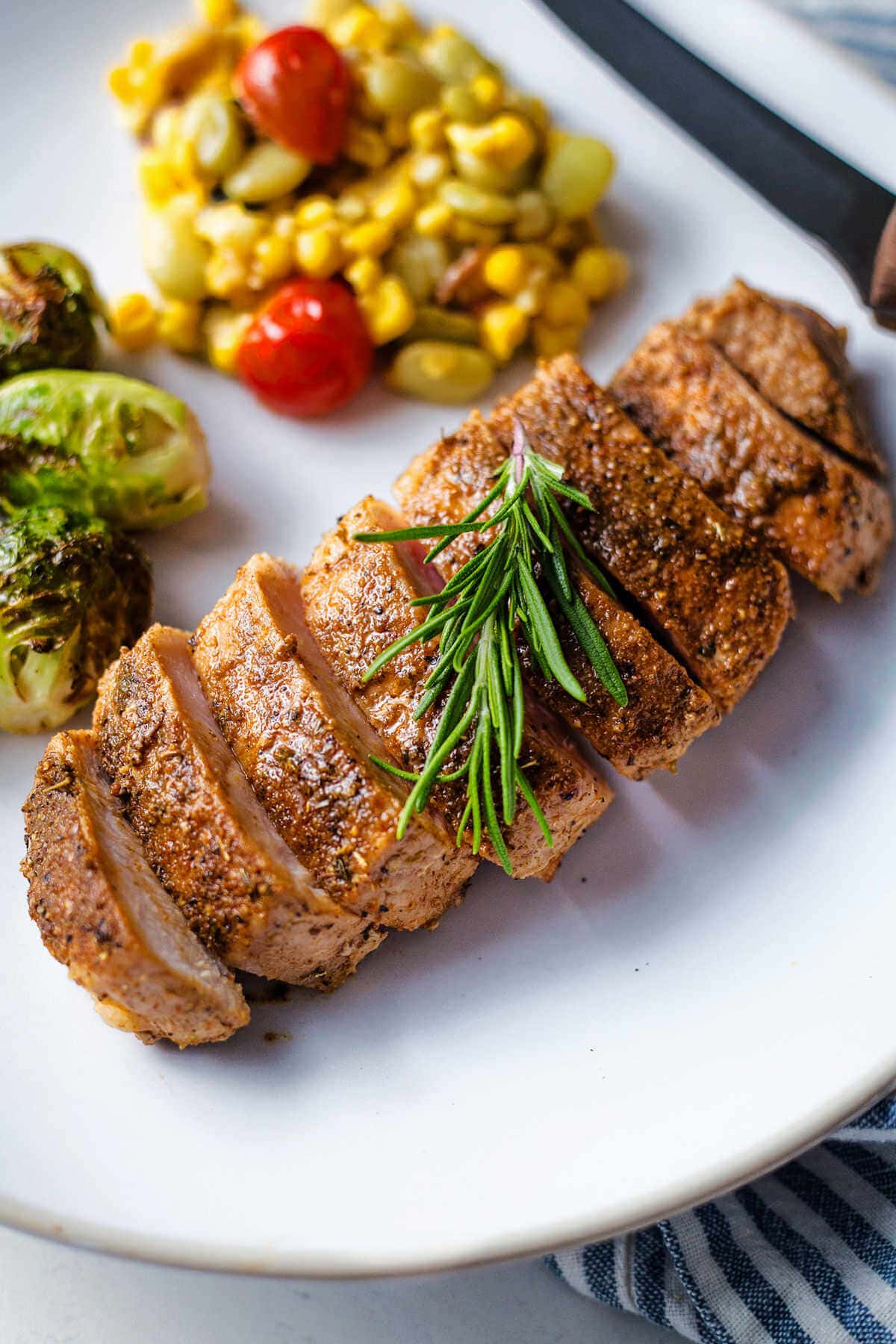 Baked pork loin chop sliced and served on a plate with vegetables.