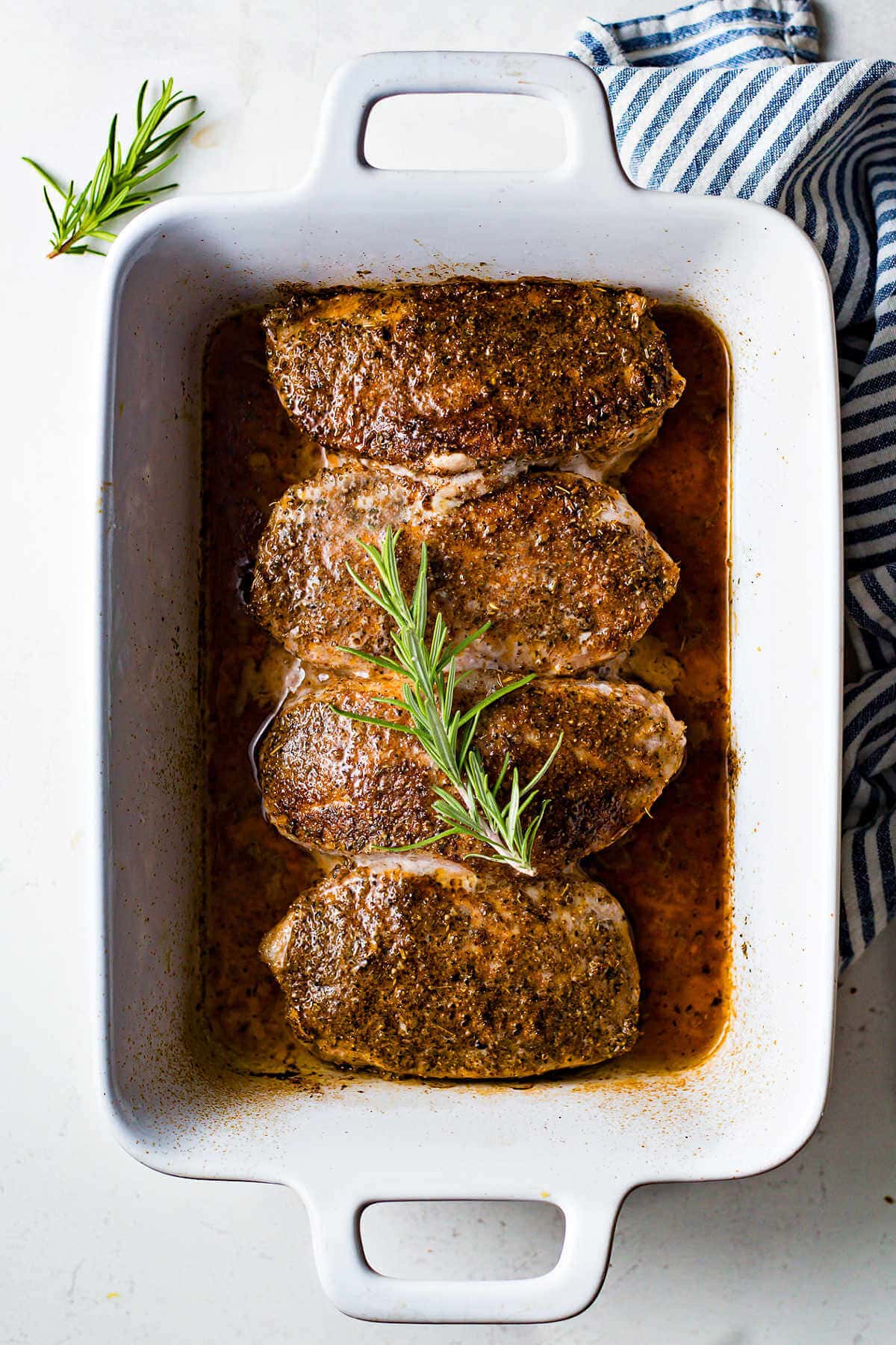 Juicy and tender baked pork loin chops in a baking dish garnished with rosemary.