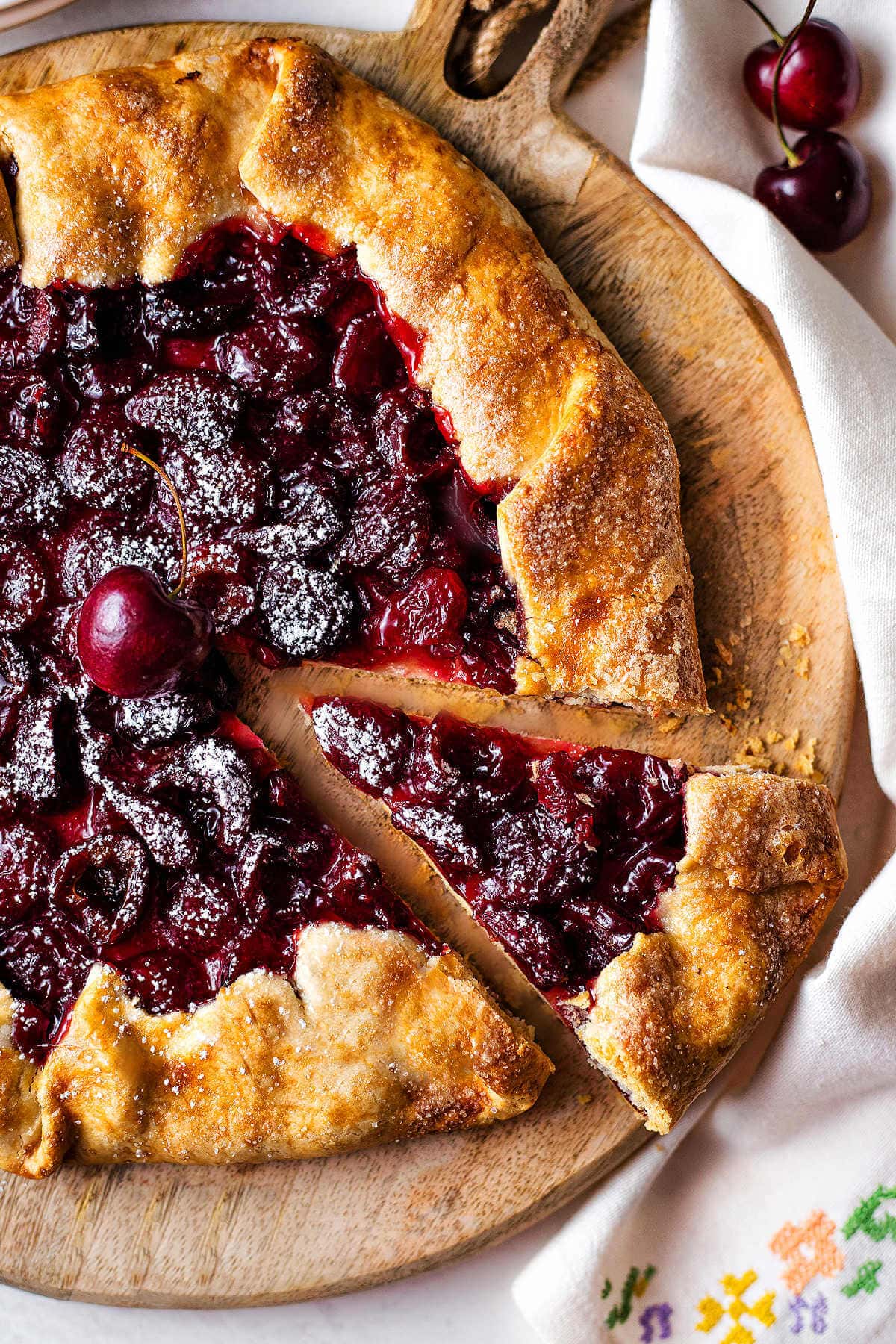 Cherry tart on a wooden board with one slice cut out.