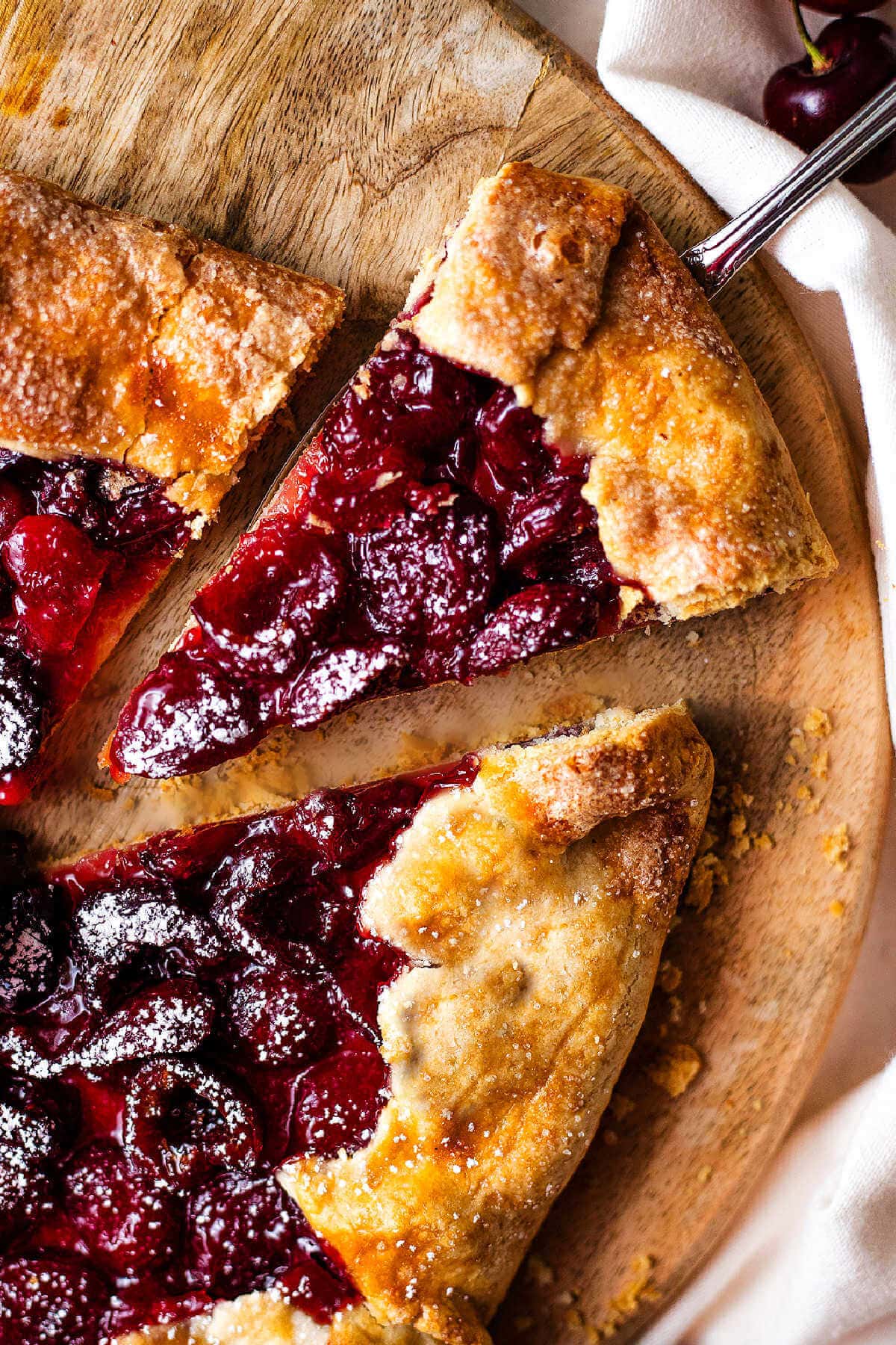 Slice of rustic cherry tart being taken by a metal spatula.