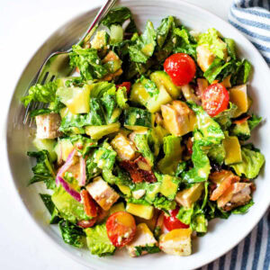 Chopped Chicken Salad in a bowl with chicken, avocado, tomatoes, cucumber, bacon, and homemade honey mustard dressing.
