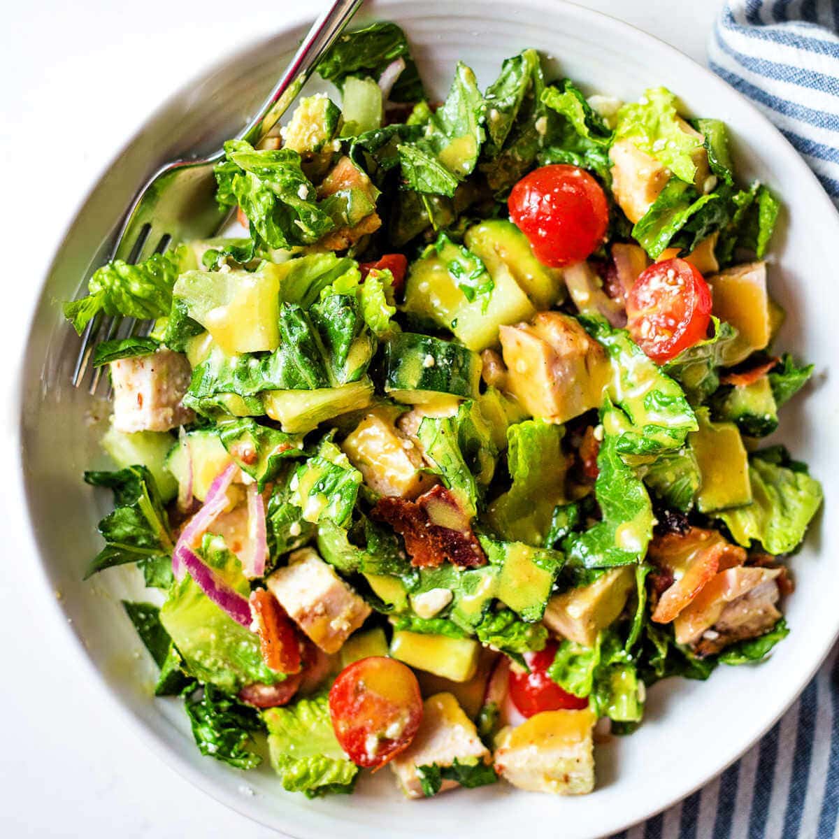 Chopped Chicken Salad in a bowl with chicken, avocado, tomatoes, cucumber, bacon, and homemade honey mustard dressing.