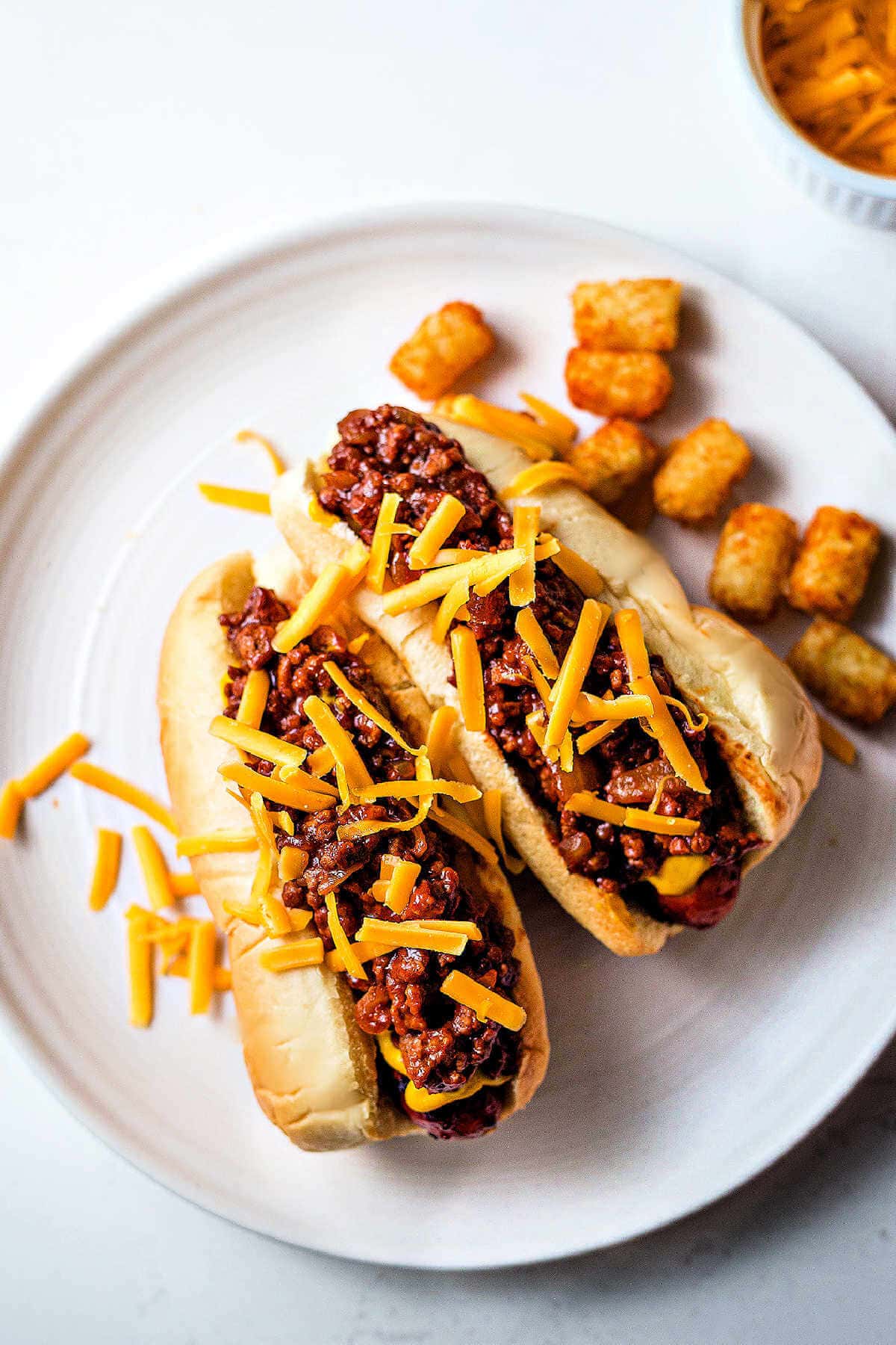 Two hot dogs on a plate topped with chili and cheese.