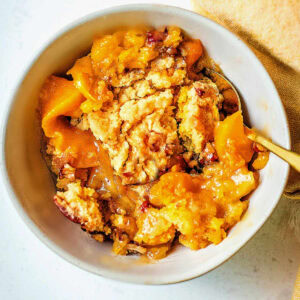Peach Dump Cake in a bowl with a gold spoon.